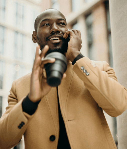 Business professional talking on the phone with a coffee cup in hand, smiling confidently outdoors. Grow up your business with IT solutions for success.