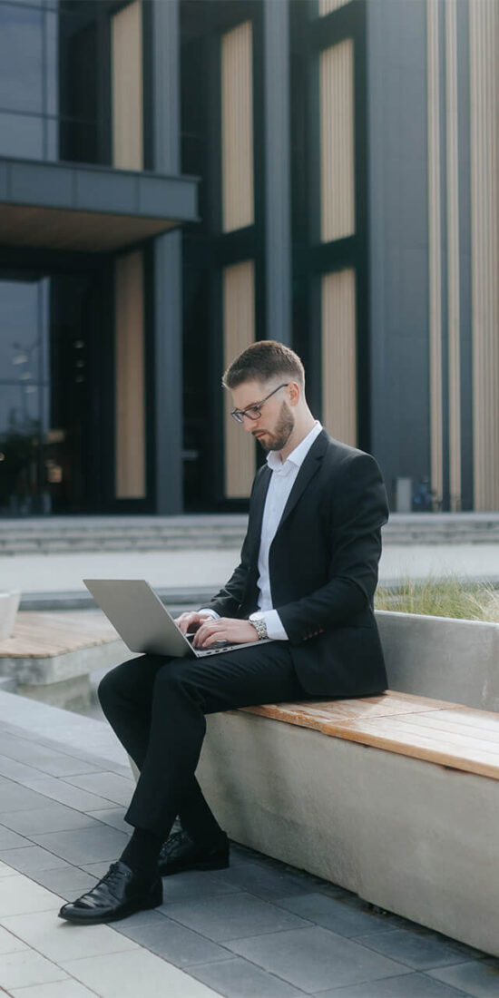 Business professional working on a laptop outside a modern office building, representing productivity and insights through Digital Analysis.