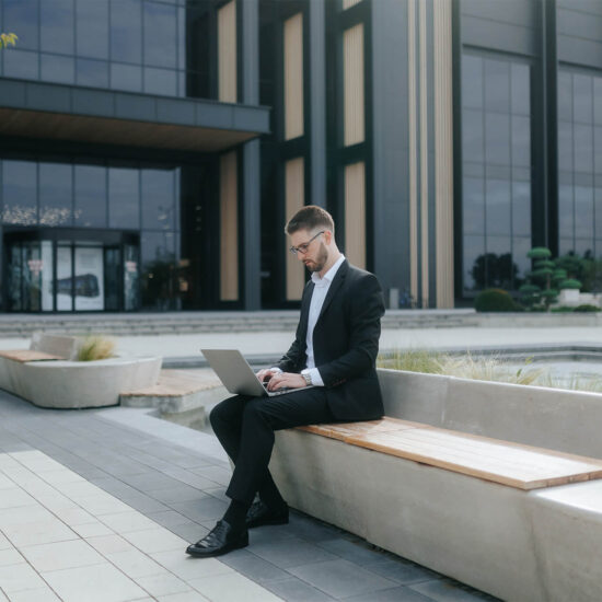 Business professional working on a laptop outside a modern office building, representing productivity and insights through Digital Analysis.