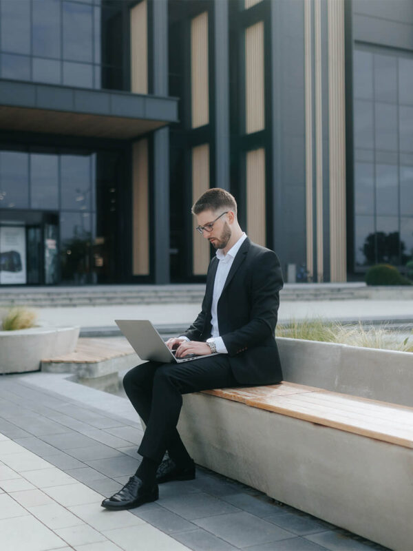 Business professional working on a laptop outside a modern office building, representing productivity and insights through Digital Analysis.