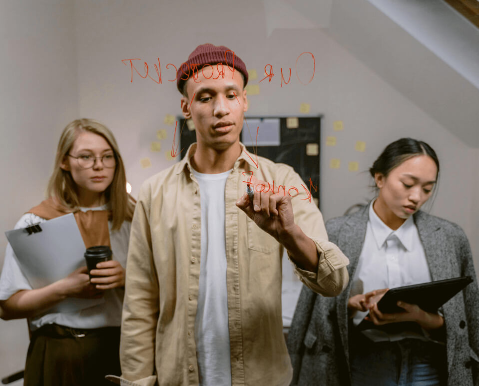 A team collaborating on Business Strategy and Planning, with one person writing on glass while others review notes and ideas for project success.
