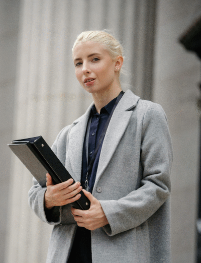 Professional woman standing confidently outdoors holding a folder, representing the dedicated and skilled UreSuccess team committed to client success.