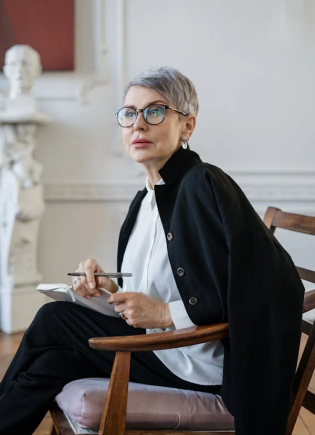 Professional woman with short gray hair and glasses sitting in a modern office space, holding a pen and notebook, symbolizing confidence and collaboration. Promotes unity and real-time financial accuracy with Stratify-Tax/VAT.